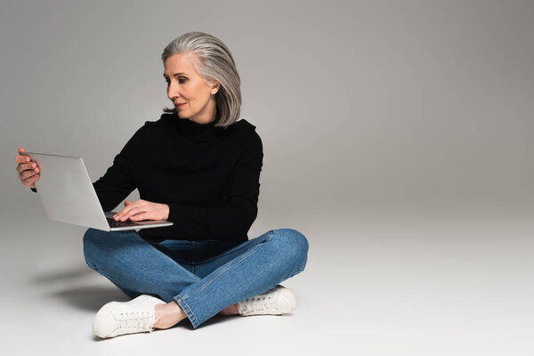 Grey haired woman using laptop on grey background 
