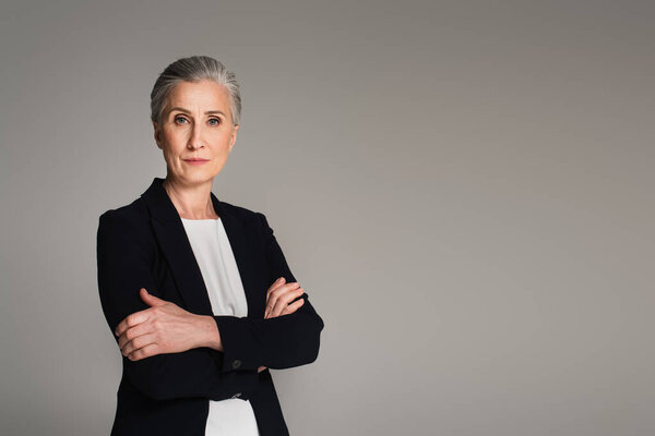 Деловая женщина средних лет со скрещенными руками, смотрящая на камеру, изолированную на сером 