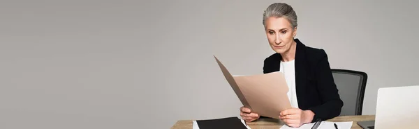 Geschäftsfrau Betrachtet Papiermappe Neben Laptop Auf Tisch Isoliert Auf Grau — Stockfoto