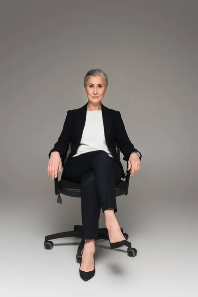 Reife Geschäftsfrau Blickt Auf Kamera Auf Bürostuhl Auf Grauem Hintergrund — Stockfoto