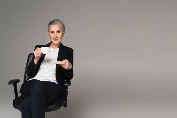 Madura Mujer Negocios Sosteniendo Taza Café Silla Oficina Aislado Gris —  Fotos de Stock