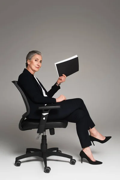 成熟的女商人把纸夹放在灰色背景的办公椅上 — 图库照片
