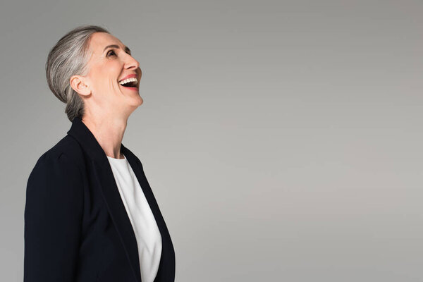 Mature businesswoman in formal wear laughing isolated on grey 