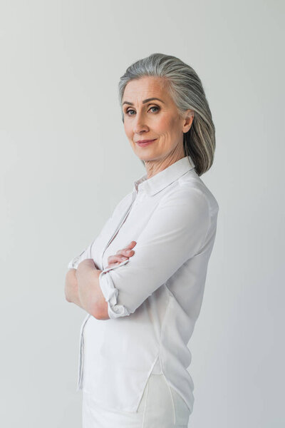 Grey haired woman in white clothes looking at camera isolated on grey 