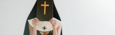 cropped view of sexy nun obscuring face with bible isolated on grey, banner clipart