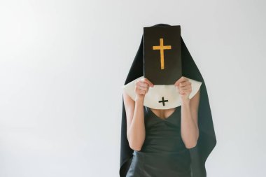 Seksi elbiseli bir rahibe. Yüzü kararmış. Kutsal İncil 'i de gri renkte.