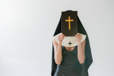 nun in sexy dress obscuring face with holy bible isolated on grey clipart