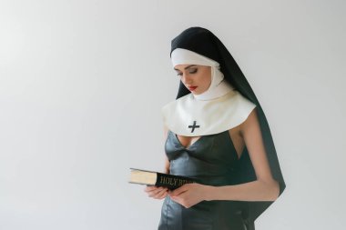 Seksi elbiseli genç rahibe kutsal İncil 'i gri renkte tutuyor.