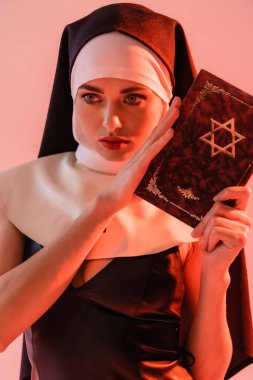 Şehvetli rahibe pembeye izole edilmiş Yahudi İncili tutuyor.