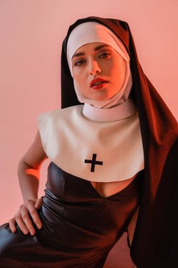 Seksi elbiseli seksi bir rahibe pembe kameraya bakıyor.