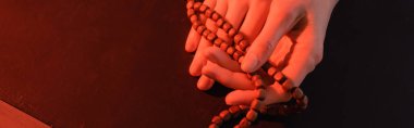 cropped view of hands of nun with prayer beads on black surface, banner clipart