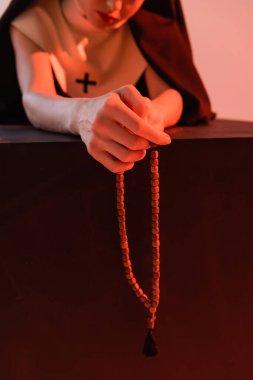 Pembe, bulanık arka planda tespih çeken rahibenin kısmi görüntüsü