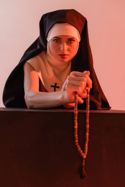 young nun looking at camera while holding prayer beads isolated on pink clipart