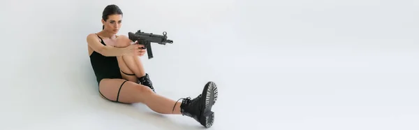 Nuori Nainen Mustassa Vartalopuvussa Tähtää Kiväärillä Istuessaan Harmaalla Taustalla Banneri — kuvapankkivalokuva
