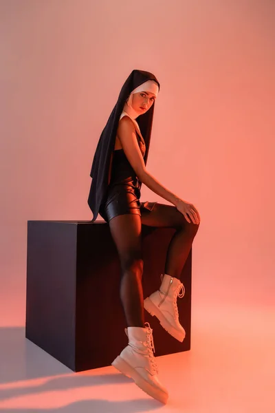 穿着皮衣和靴子的性感修女 穿着粉色背景的黑色立方体 — 图库照片