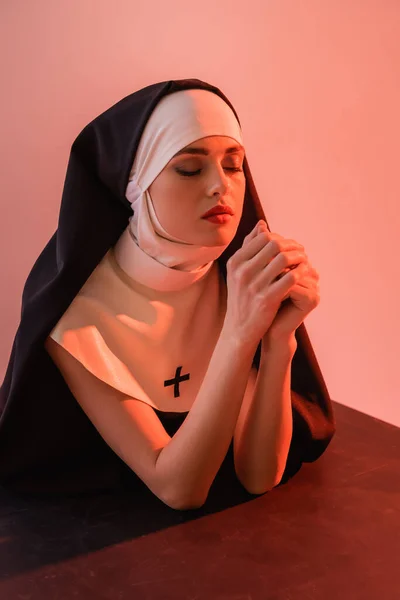年轻修女在黑色表面上闭着眼睛祈祷 与粉色隔离 — 图库照片