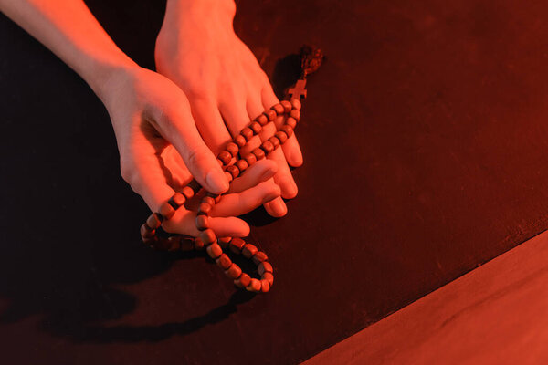 partial view of woman holding rosary on black surface 
