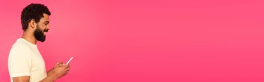 Pembe pankartta izole edilmiş akıllı telefon kullanan mutlu Afro-Amerikan adamın yan görüntüsü