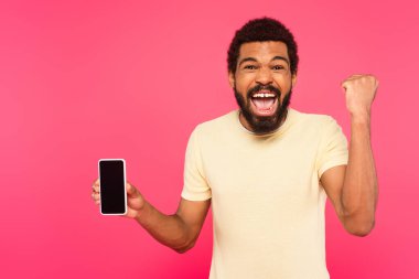 Heyecanlı Afro-Amerikan tişörtlü adam elinde pembe ekranlı akıllı telefon tutuyor.