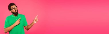 Şok olmuş gözlüklü Afro-Amerikan adam pembe pankartta izole edilmiş parmaklarıyla işaret ediyor.