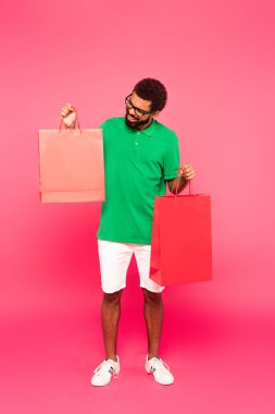 Gözlüklü, yeşil polo tişörtlü ve pembe çantalı mutlu Afro-Amerikan bir adam.
