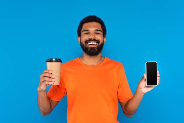 Mutlu Afro-Amerikalı adam elinde kağıt bardak ve mavi ekranlı akıllı telefon tutuyor.
