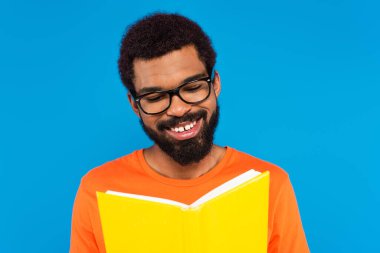 Mutlu Afro-Amerikan adam mavi üzerine izole kitap okuyor.