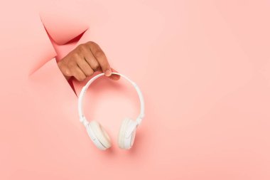 Pembe arka planda kablosuz kulaklık tutan Afro-Amerikan bir adamın kısmi görüntüsü