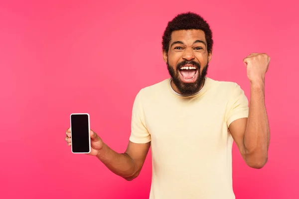 興奮アフリカ系アメリカ人男性でTシャツを着てスマートフォンを持っていますピンクの画面に隔離された — ストック写真