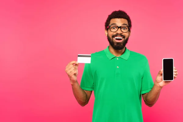 ピンクで隔絶されたスマートフォンやクレジットカードを持っているアフリカ系アメリカ人男性が — ストック写真