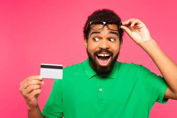 戴着眼镜的令人惊讶的非洲裔美国人看着用粉色隔离的信用卡 — 图库照片