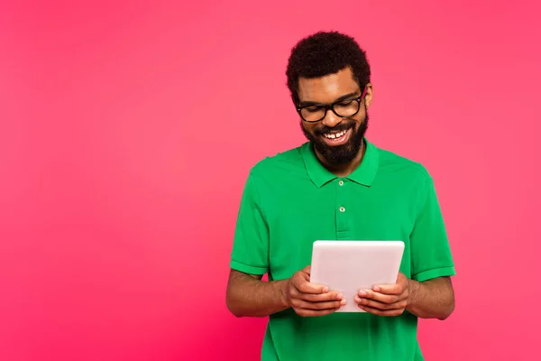 身穿眼镜和绿色马球衫的快乐的非洲裔美国人 用数字平板电脑在粉色上进行隔离 — 图库照片