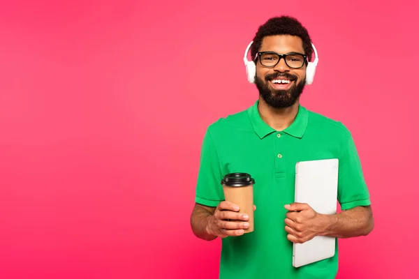 幸せなアフリカ系アメリカ人男性の眼鏡と緑のポロシャツ紙コップを持っていますノートパソコンでピンクに隔離された — ストック写真