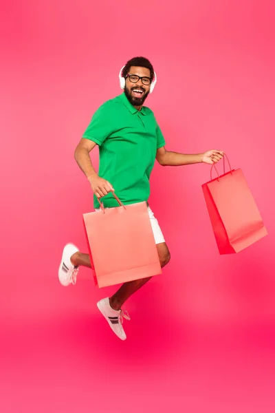 全身上下都是兴奋的非洲裔美国人 戴着眼镜和耳机 手里拿着粉色购物袋 — 图库照片
