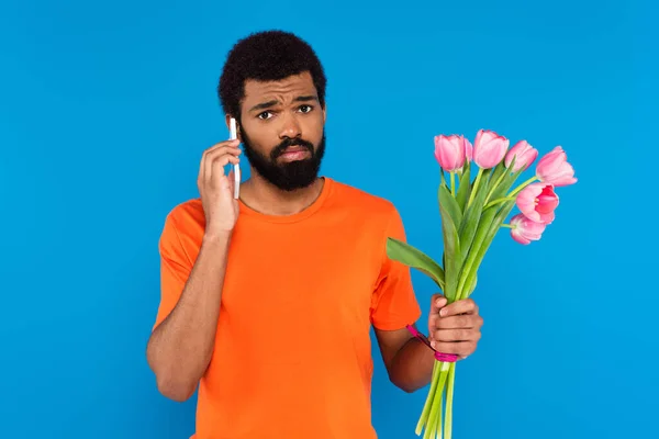 분홍색 튤립을 파란색으로 고립된 스마트폰으로 얘기하는 아프리카 미국인 — 스톡 사진