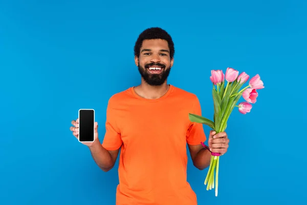 Happy African American Man Holding Pink Tulips Smartphone Isolated Blue — Stock Photo, Image