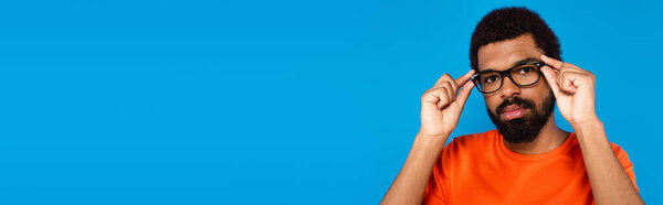 bearded african american man adjusting glasses isolated on blue, banner