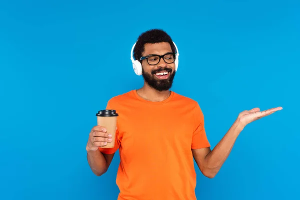 快乐的非洲裔美国人 戴着无线耳机 一边听音乐 一边拿着蓝色的纸杯 — 图库照片