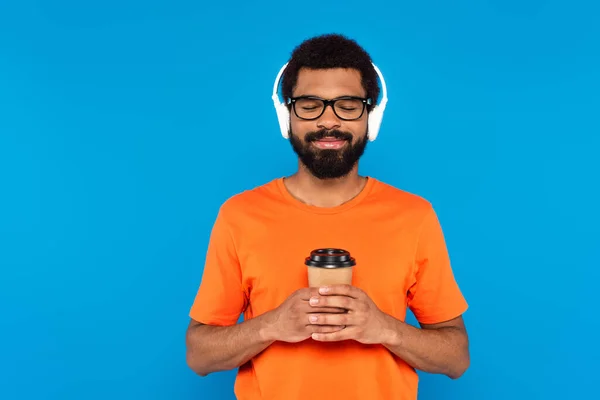 青で隔絶された紙コップを持っているワイヤレスヘッドフォンで楽しいアフリカ系アメリカ人男性 — ストック写真