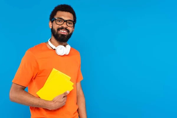 Glimlachende Afro Amerikaanse Man Draadloze Koptelefoon Met Boeken Geïsoleerd Blauw — Stockfoto