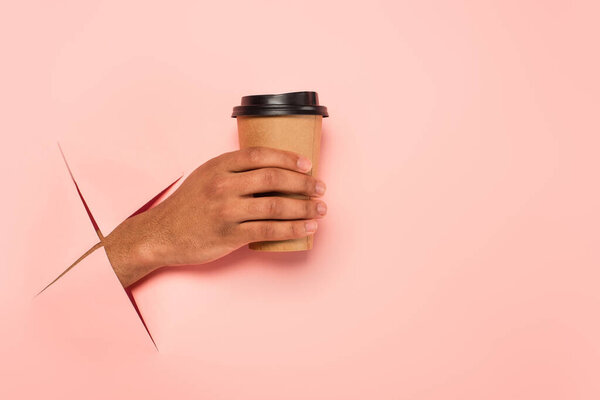 partial view of african american man holding paper cup on ripped pink background 