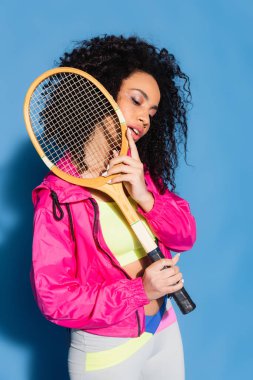 Genç Afro-Amerikalı kadın mavi tenis raketiyle poz veriyor.