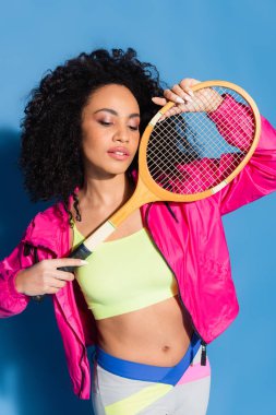 Kıvırcık Afro-Amerikalı kadın. Üstünde tenis raketi, üstünde mavi...