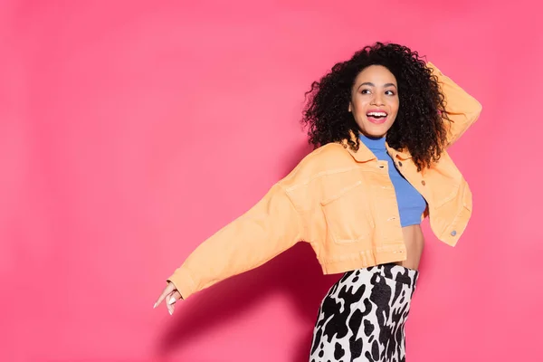 excited african american woman in crop top and jacket on pink