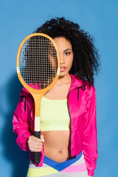 若いアフリカ系アメリカ人女性がテニスラケットを着て青いカメラを見て — ストック写真