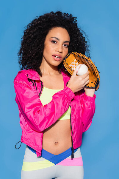 curly african american woman in leather glove holding baseball on blue