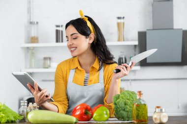 Sebzelerin yanında yemek tarifi izlerken dijital tablete bakan mutlu genç bir kadın. 