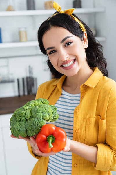 happy brunette woman holding ripe green broccoli and red bell pepper
