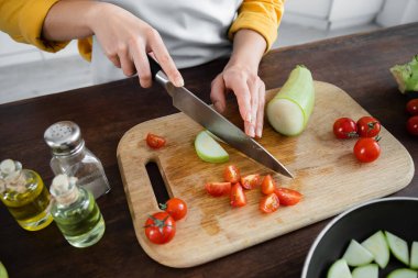 partial view of woman cutting zucchini near sliced cherry tomatoes on chopping board  clipart