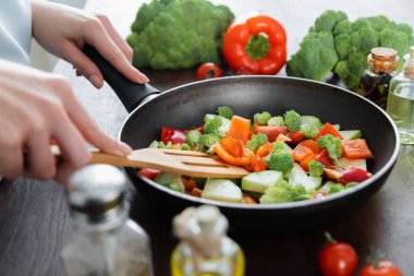 Kızartma tavasında dilimlenmiş sebzeleri spatulayla karıştıran kadının kısmi görüntüsü 